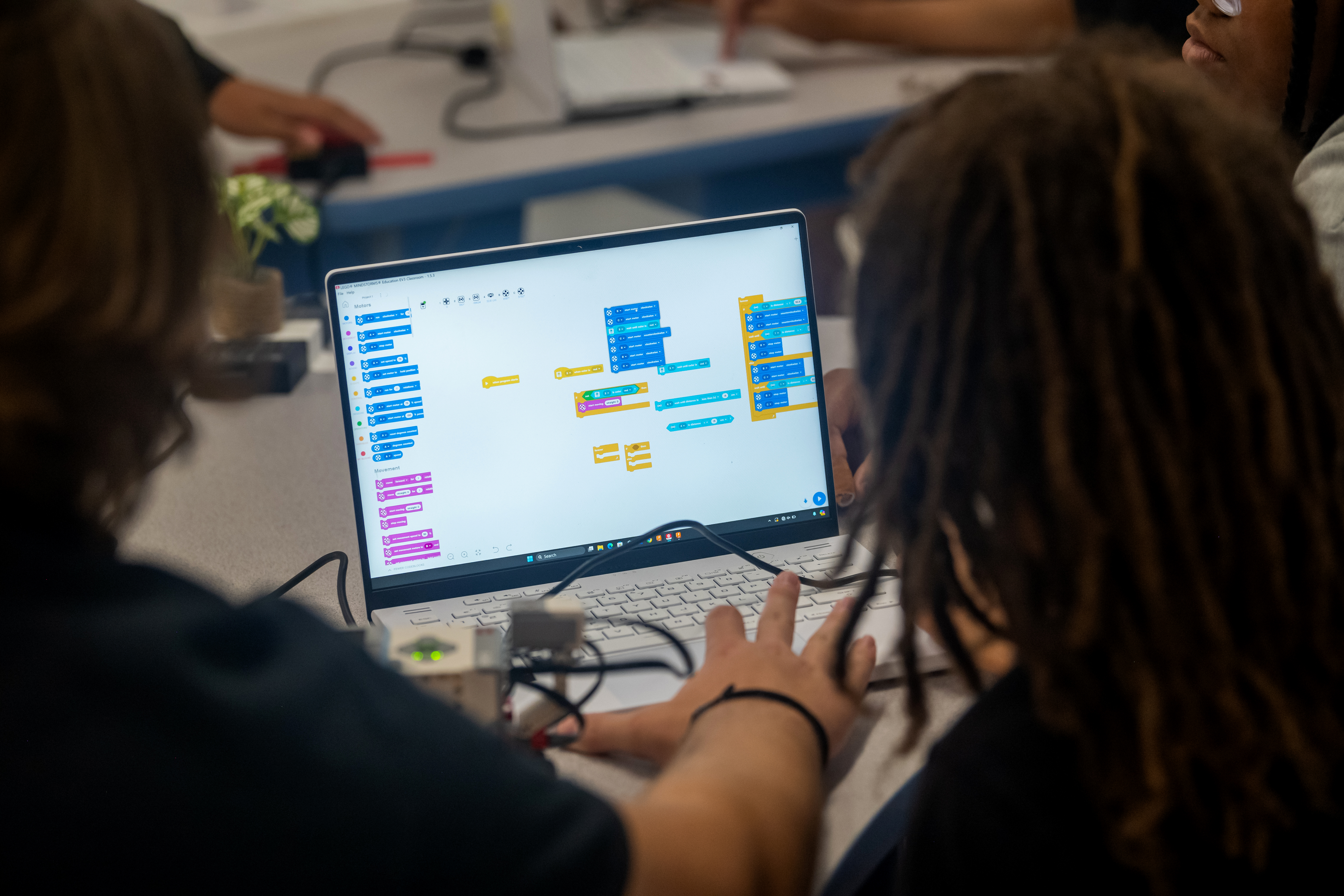 The camera points over the shoulders of two high school students and focuses on the laptop screen they're looking at. On the screen are many colorful "blocks" of code.